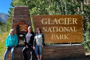 Two women and a man standing in front of a Glacier National Park sign