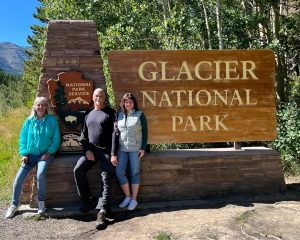 Two women and a man standing in front of a Glacier National Park sign