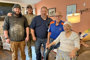 Four men standing next to a woman sitting in a chair