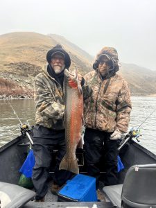 Two men in a boat holding a large steelhead trout