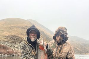 Two men in a boat holding a large steelhead trout